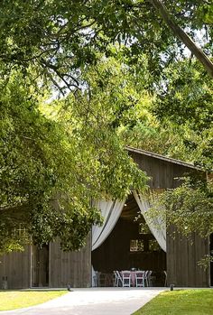 the barn is surrounded by lush green trees and white drapes on it's windows