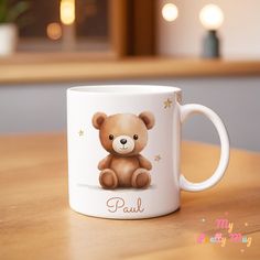 a brown teddy bear sitting on top of a wooden table next to a white mug