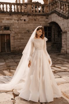 a woman wearing a wedding dress and veil standing in front of an old stone building