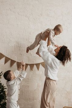 a woman holding a baby up in the air while standing next to a little boy