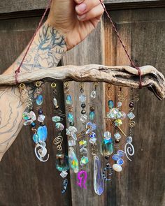 a person holding up a piece of wood with many different colored beads hanging from it