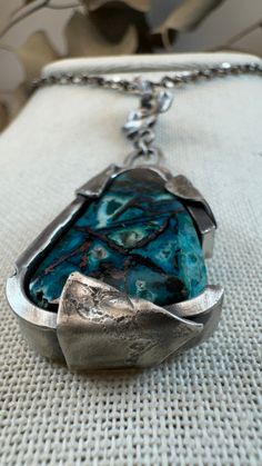 This stunning handcrafted piece highlights the natural beauty of Chrysocolla with native copper. This unique pendant features a live-edge Chrysocolla stone, its vibrant turquoise and teal hues accentuated by rich copper veins, creating a harmonious blend of earthy tones and calming energy. The stone is securely encased in a custom sterling silver setting designed to mimic the organic shapes of nature, making this piece both elegant and bold. Each necklace is meticulously crafted with intention, Unique Turquoise Necklace With Patina, Turquoise Chrysocolla Necklace With Patina, Chrysocolla Necklaces With Natural Stones, Unique Turquoise Jasper Jewelry, Unique Chrysocolla Necklace With Natural Stones, Nature-inspired Patina Pendant Jewelry, Unique Hand Forged Turquoise Necklace, Artisan Chrysocolla Jewelry For Collectors, Artisan Necklace With Patina For Collectors