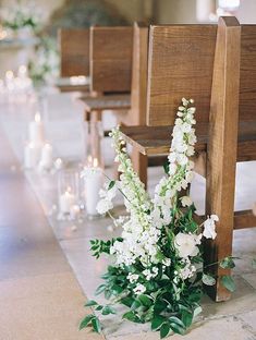 white flowers and greenery sit on the pews at a wedding ceremony with candles in the background