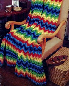 a colorful crocheted blanket sitting on top of a chair next to a basket