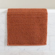 an orange crocheted towel hanging on the wall in a white bathroom with marble flooring