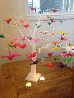 a white tree with colorful origami birds hanging from it's branches on a wooden table