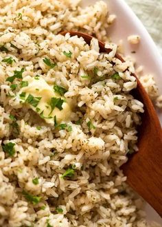 a white plate topped with rice and parsley next to a wooden spoon on top of a table