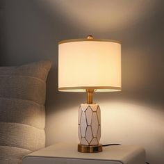 a table lamp sitting on top of a white ottoman next to a bed with pillows