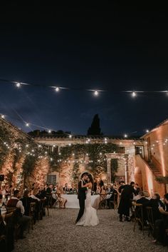 a bride and groom share their first dance under string lights in an outdoor courtyard at night