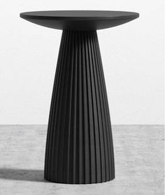 a black round table sitting on top of a cement floor next to a white wall