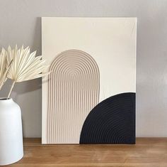 a white vase sitting on top of a wooden table next to a black and white painting