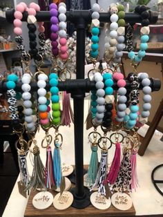 several different colored beads and tassels hanging from a black stand in a store