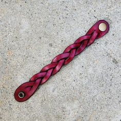 a purple braided object is laying on the ground in front of a concrete wall