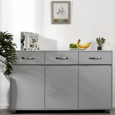 a grey sideboard with two bananas on top and some plants in the corner next to it