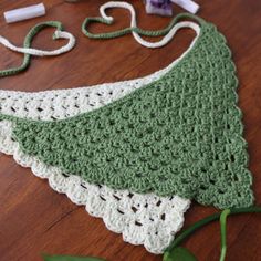 a crocheted green and white piece of cloth on a wooden table next to scissors