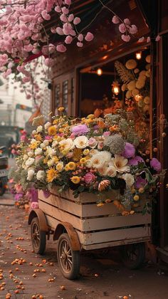 a wooden cart filled with lots of flowers on the side of a street next to a building