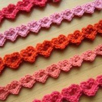 several crocheted ribbons are lined up on a wooden surface, one is pink and the other is orange