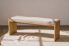 a wooden bench sitting on top of a white rug in front of a wall and floor