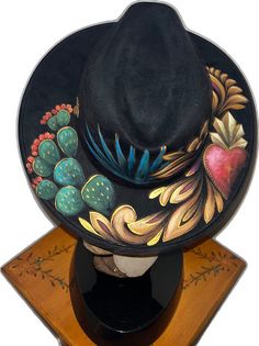 a black hat is sitting on top of a wooden stand and has colorful flowers painted on it