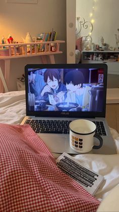 an open laptop computer sitting on top of a bed next to a cup and saucer