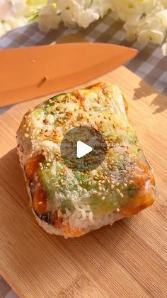 a piece of food on a cutting board with a knife next to it and flowers in the background