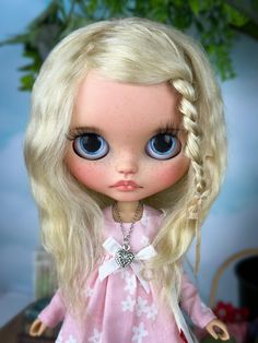 a doll with blonde hair and blue eyes wearing a pink dress, braided in