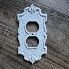 an ornate white light switch plate on a wooden floor