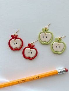 three apple shaped earrings next to a pencil