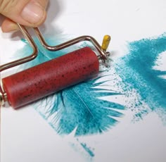 a person is painting feathers with blue and red colors on the paper while holding a paint roller in their hand