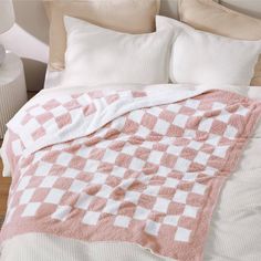 a pink and white checkered blanket on top of a bed next to two pillows