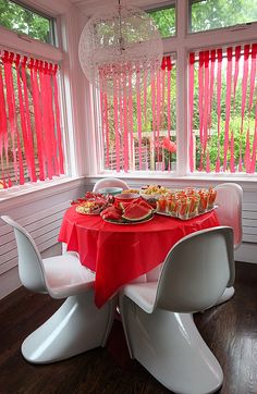 a red table cloth is on top of the white chairs in front of the windows