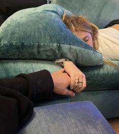 a woman laying on top of a blue couch next to a person with her arm wrapped around a pillow