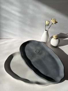 two vases with flowers in them sitting on a table next to an oval shaped tray