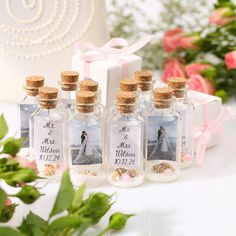 four small bottles filled with sand next to flowers and a gift box on a table