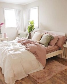 a bed with pink sheets and pillows in a bedroom next to a table, chair and window