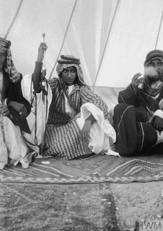 three men sitting on the ground in front of a tent with white drapes