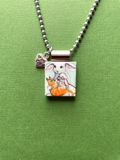 a small square pendant with a dog and cat on it's side, hanging from a ball chain