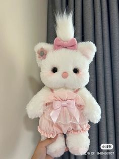 a hand holding a white teddy bear with pink bows on it's head and tail