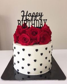 a white and black cake with red roses on the top is decorated with happy birthday lettering