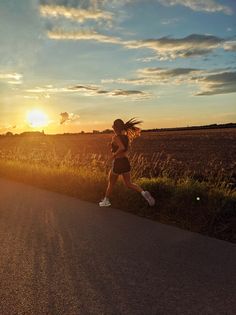 a woman running down the road in front of the sun at sunset with her hair blowing in the wind