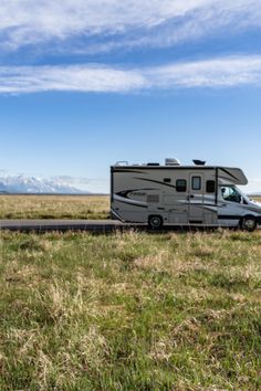 an rv is parked on the side of the road in front of mountains and grass