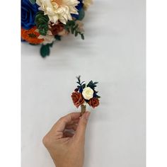 a hand is holding a fake flower in front of two flowers on the wall,