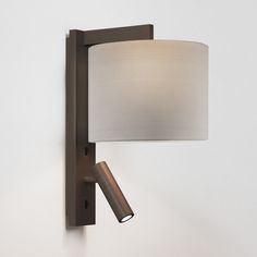 a wall light with a white shade on the side and a brown metal pole attached to it