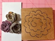 some paper flowers are sitting on top of a piece of crafting material next to a cutting board