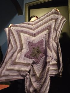 a woman is holding up a crocheted blanket