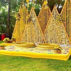 a yellow table topped with plates covered in flowers and chains on top of grass next to trees