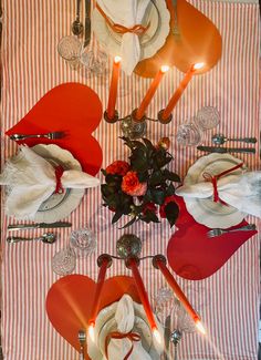 the table is set with red and white plates, silver utensils and candles