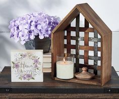 a wooden house shaped candle holder next to a vase with purple flowers and a greeting card