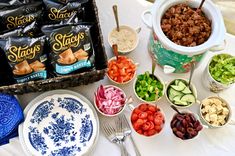 a table topped with bowls and plates filled with different types of food next to containers of chips