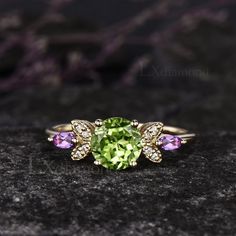 a ring with an oval cut peridot surrounded by three smaller round diamonds on a black surface